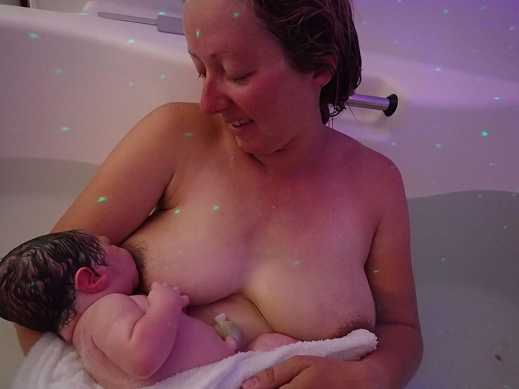 A photograph of a new mother breastfeeding her baby in the water where she gave birth