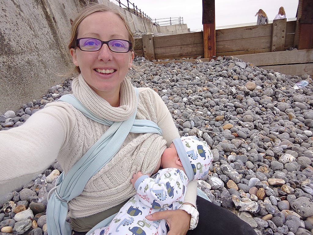 A woman looking at the camera while breastfeeding he small baby on a stony beach