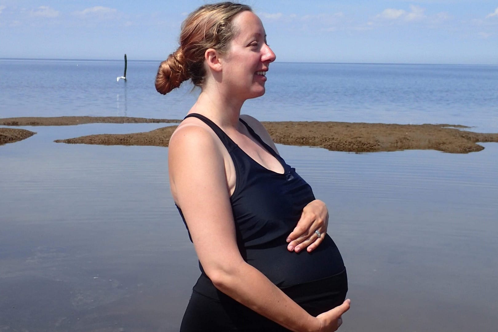 A photograph of a pregnant mother in a swimming costume standing by the sea