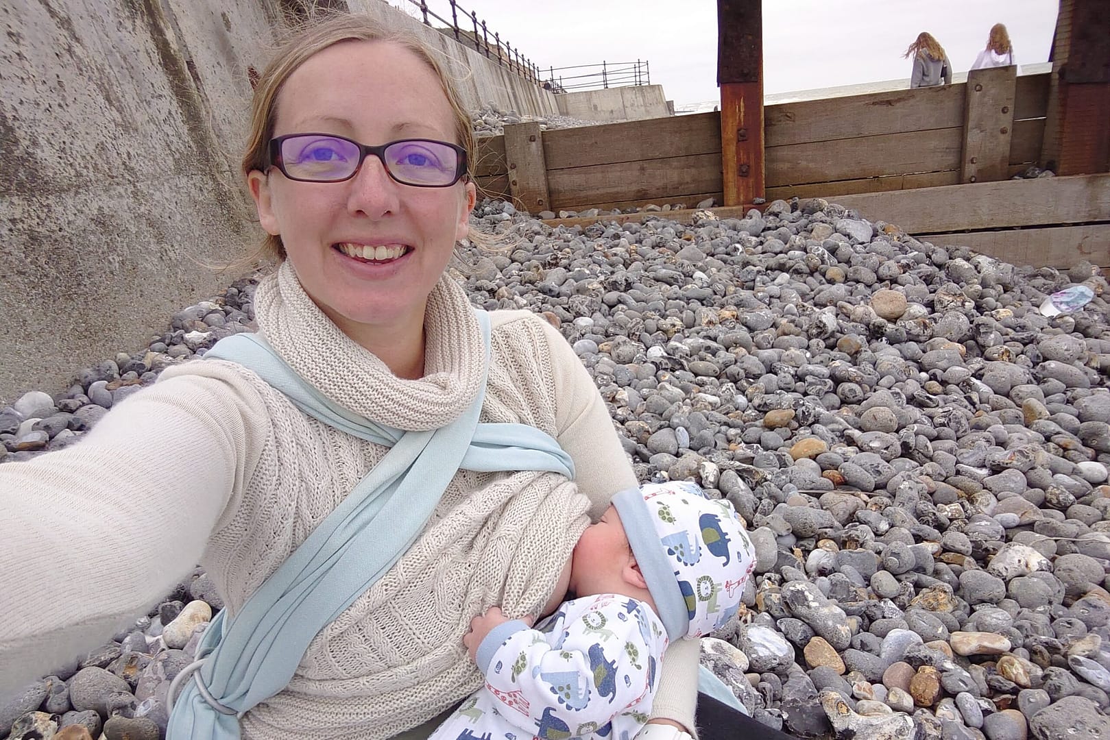 A mother breastfeeding a baby on a stone beach