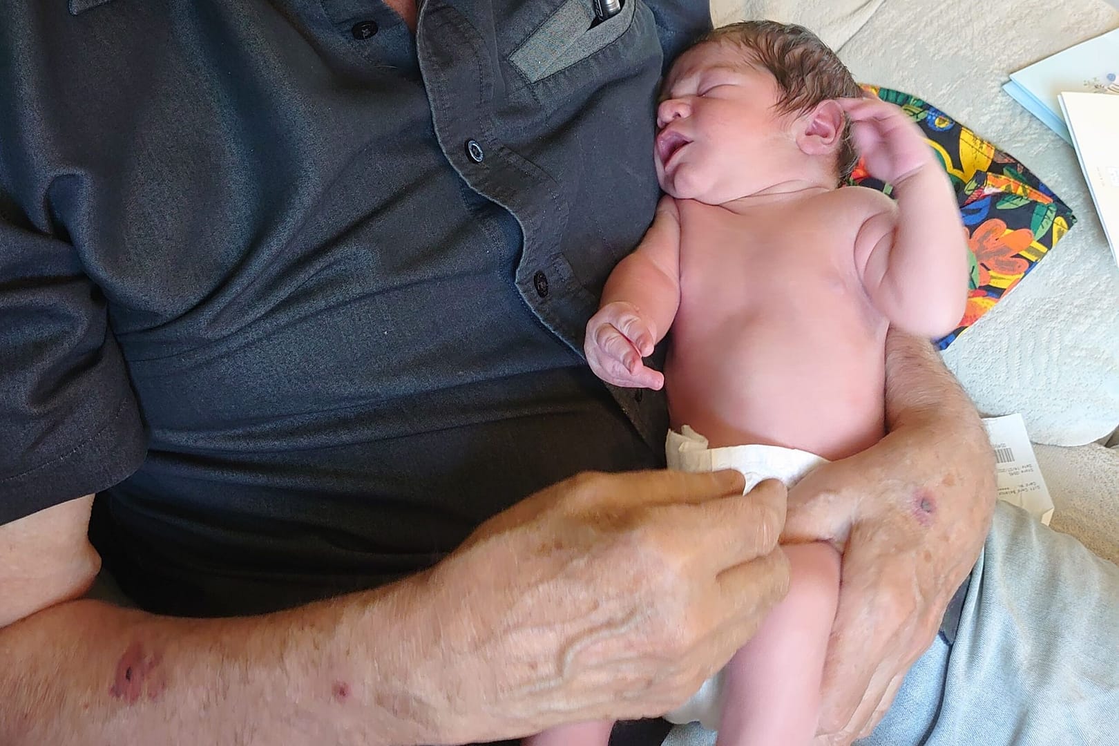 A baby in his nappy, being held by his grandad
