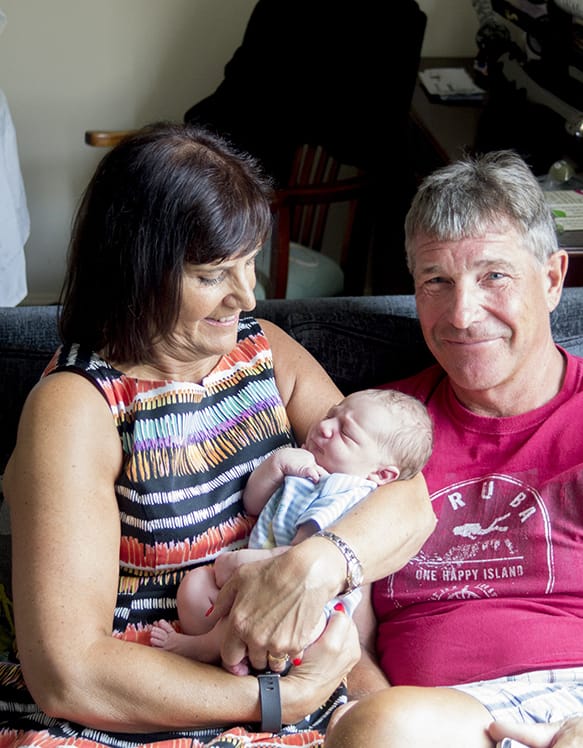 A portrait image of a new-born being held by their grandparents. Handling visitors.