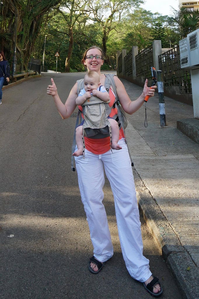 A mum with her child in a Ergobaby 360 standing on a street, giving two thumbs up