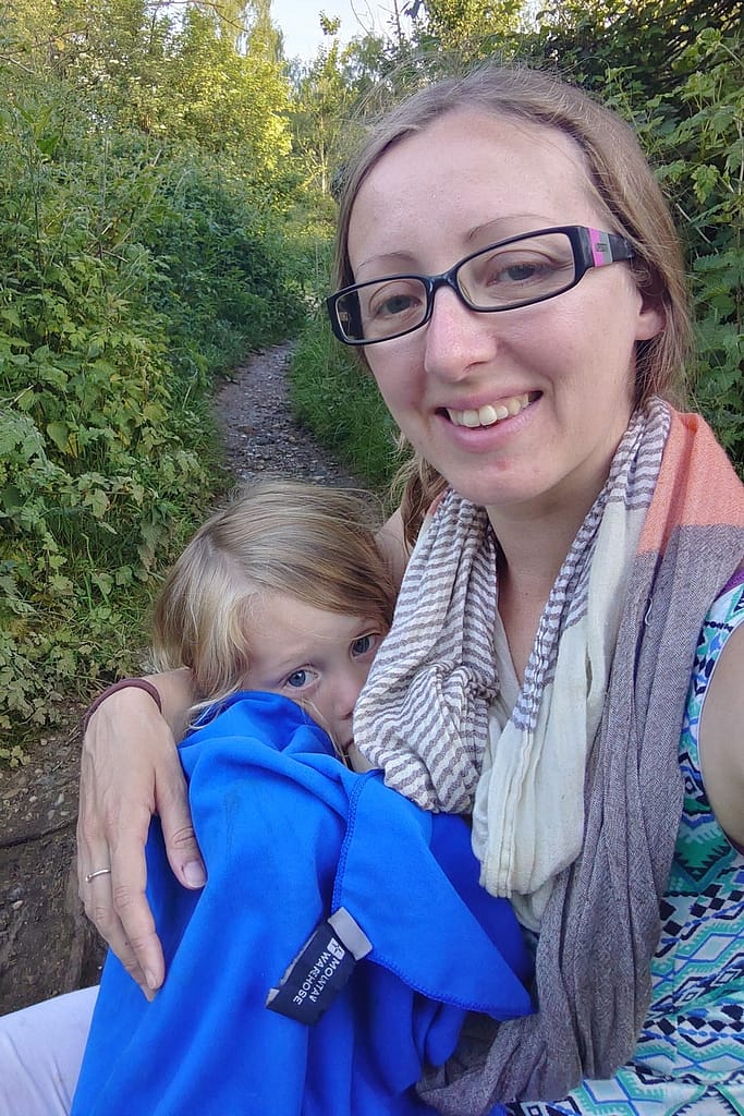 A mother natural term breastfeeding her 3 year old outside in nature. The child is wrapped in a blue towel.